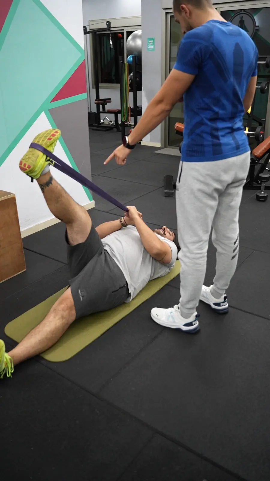 A coach assisting a client with a band stretch on the floor