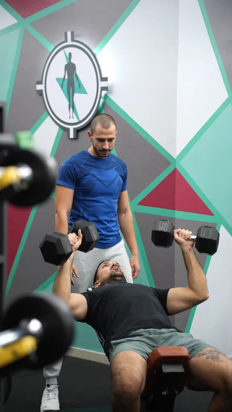 A coach guiding a client on the bench press at Wellbe Health Center